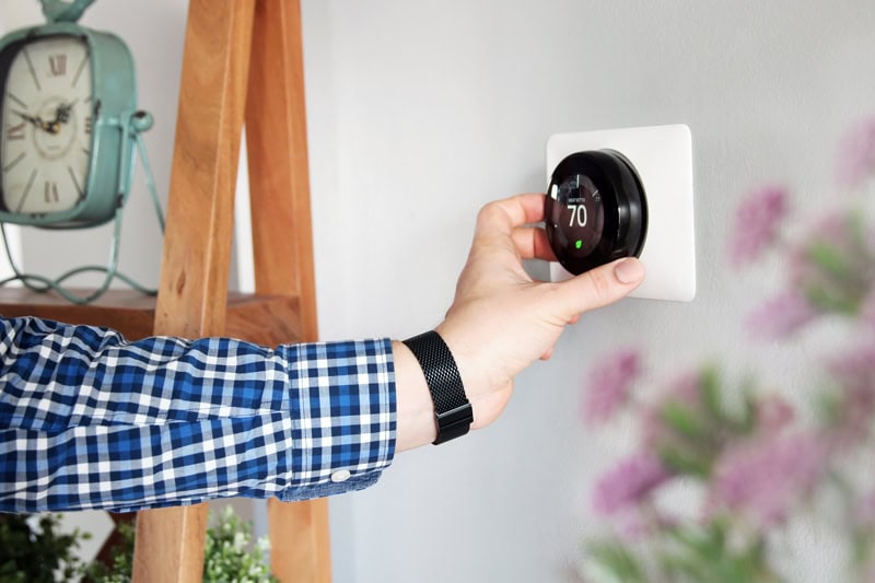 Hand adjusting a smart thermostat on a wall to set home temperature for comfort and energy efficiency