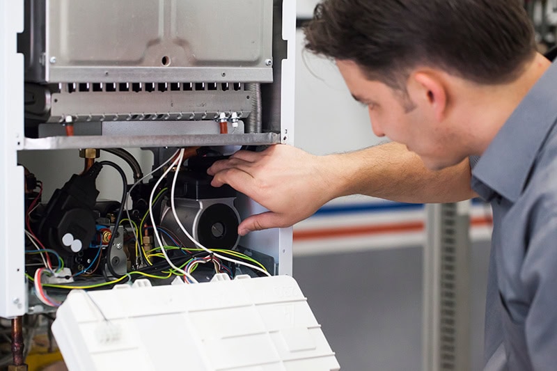 4 Important Heat Pump Maintenance Tips. A man working on a heat pump.