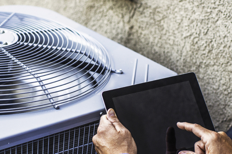 Maintenance engineer using digital tablet to inspect air conditioning unit and provide summer cooling tips.